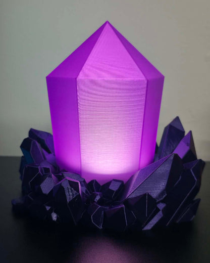 A purple 3D-printed crystal lamp glowing from within, resting on a dark, faceted base against a plain light gray background.
